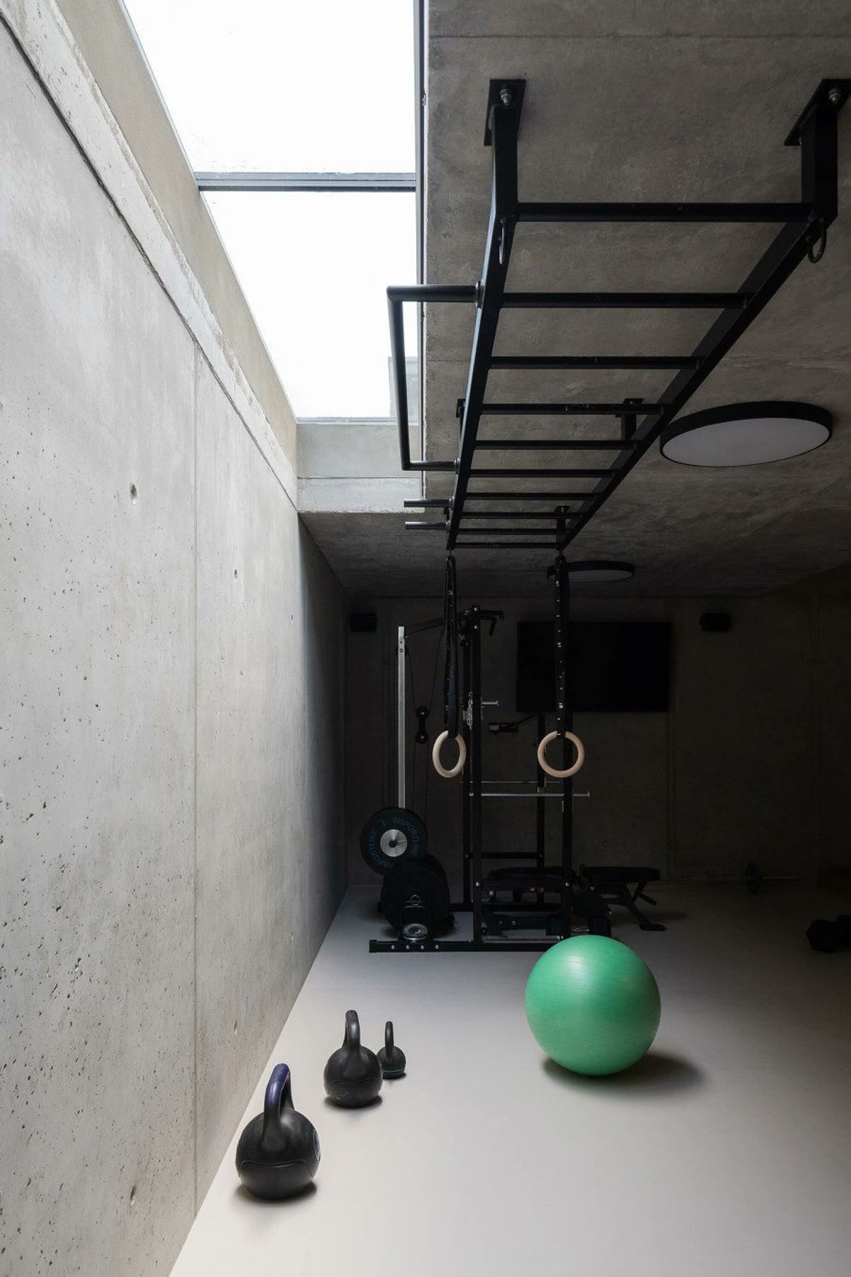 A concrete home gym with kettlebells, rings, and a pull-up ladder