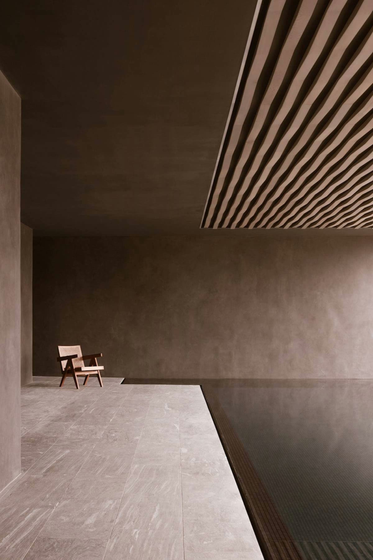 A spare spa lounge with a wooden chair beside a dark indoor pool