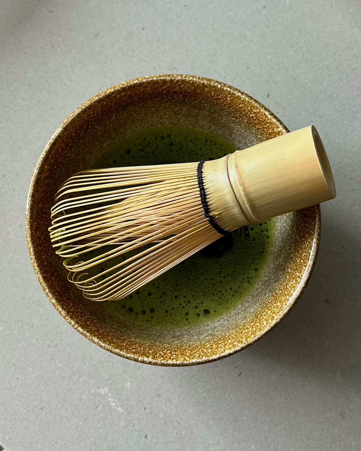 A ceramic bowl of whisked matcha with a bamboo chasen
