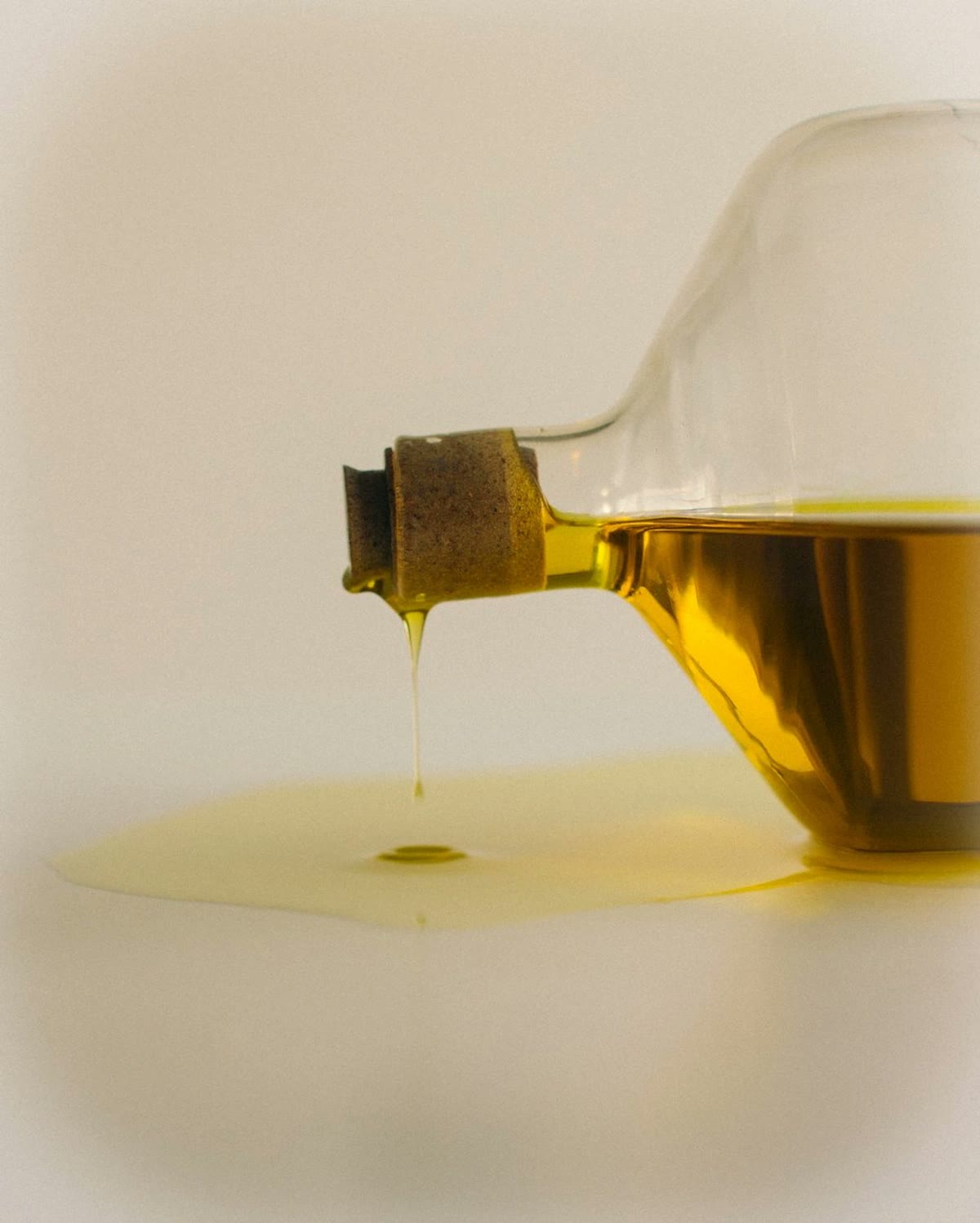 Olive oil dripping from a glass bottle onto a white surface