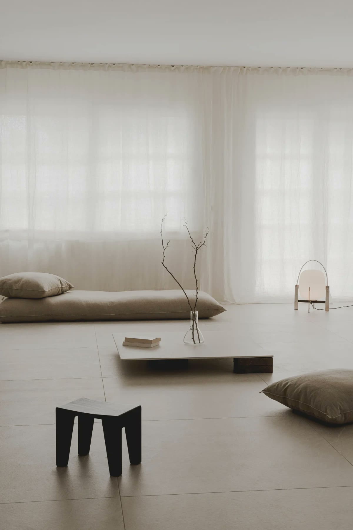 A spare rest room with linen daybed, sheer curtains, and a low table